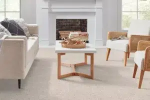 Living room with a white coffee table, beige sofa, and wicker chairs around a stone fireplace; a basket and books sit on the table.