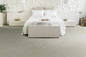 French Silk | The Design Emporium Minimalist bedroom with white bedding, beige ottoman at the foot of the bed, and built-in nightstands; textured white wall behind the bed with neutral decor.