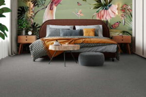 Lagoon | The Design Emporium Bedroom with tropical mural behind a brown upholstered bed, orange throw, gray patterned blanket and assorted pillows; round wooden coffee table, gray pouf, two wooden nightstands, and plants.