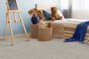 Point Break | The Design Emporium Wooden easel with chalkboard in a pastel blue kids' room, beside a bed with a teddy bear and round wooden stools stacked with books and pencils.