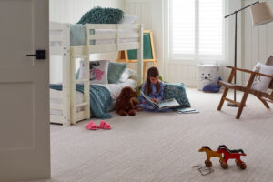 Yuma | The Design Emporium Girl sits on a beige carpet reading a book in a bright kids' bedroom beside a white bunk bed with a dog nearby.
