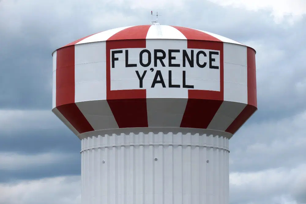 Water tower with red and white stripes reading 'FLORENCE Y'ALL' against a cloudy sky.